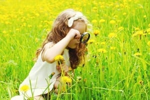 Little girl playing magnifying glass in grass