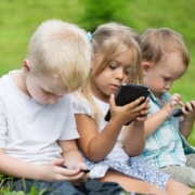 Happy children using smartphones sitting on the grass in the park.