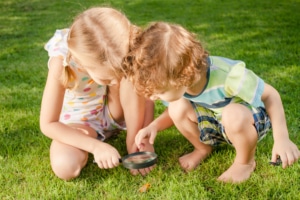 Two little kids playing with magnifying glass outdoors